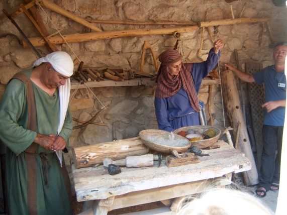 A carpenter demonstrates a few replicas of first-century woodworking tools, including a plane and a drill. The woman is showing how wool was spun into thread, to be woven on a loom.